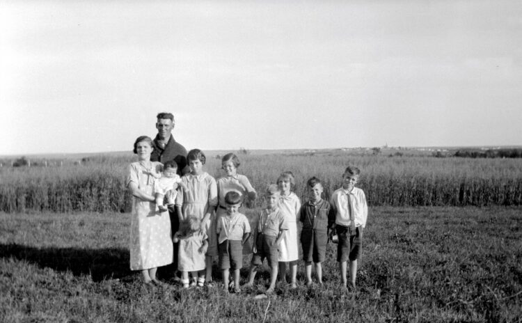 Famille comprenant les deux parents et leurs 9 jeunes enfants posant en plein air devant un champ en culture.