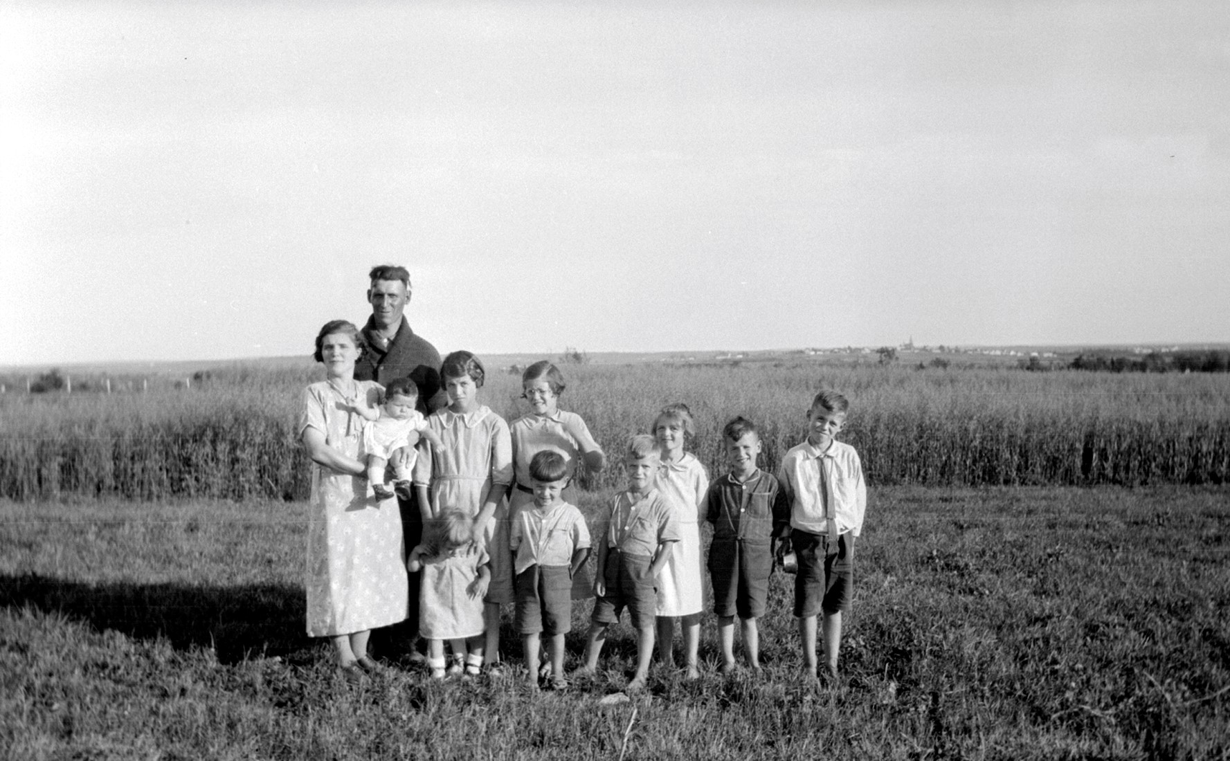 Famille comprenant les deux parents et leurs 9 jeunes enfants posant en plein air devant un champ en culture.