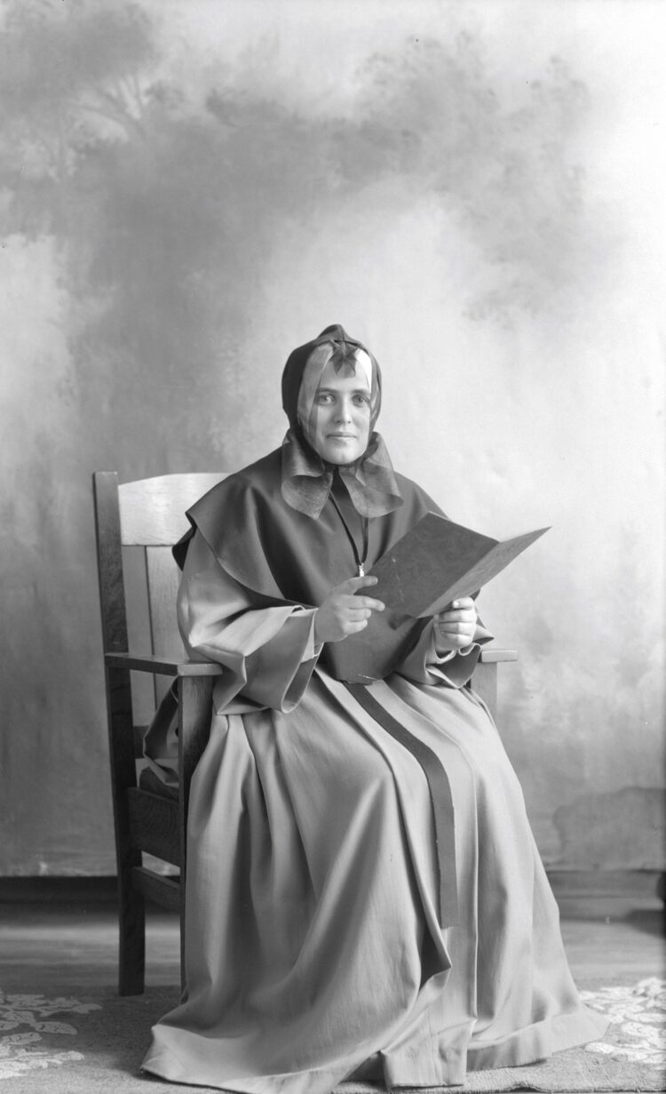 Portrait de studio de Berthe Dumont en habits de religieuse et tenant un carnet ouvert.
