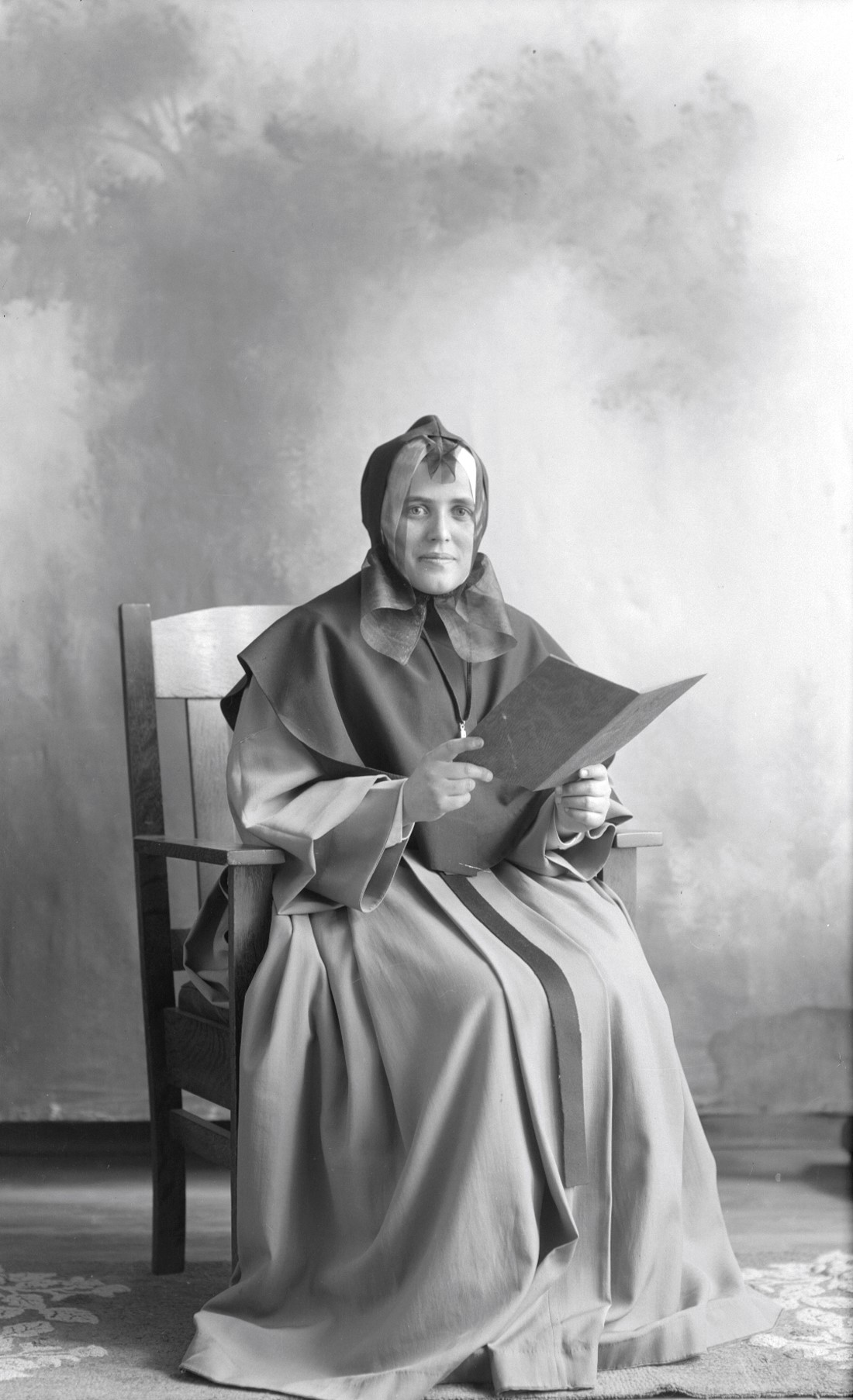 Portrait de studio de Berthe Dumont en habits de religieuse et tenant un carnet ouvert.