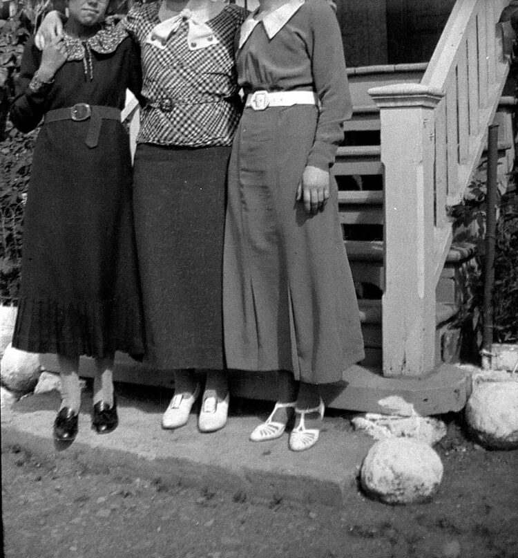 Trois jeunes femmes bras dessus bras dessous au pied d'un perron et dont les visages sont hors du cadre.