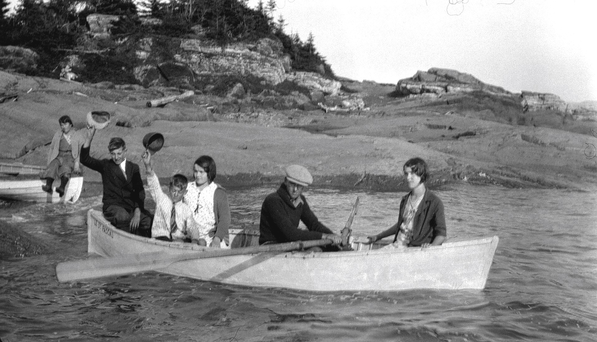 Trois garçons et deux filles dans une petite embarcation prenant le large sous le regard d'une femme.