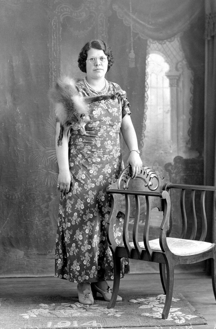 Portrait de studio d'une femme revêtant une robe fleurie et une fourrure de renard argenté sur son épaule droite.