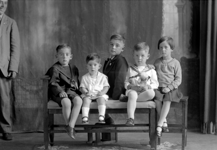 Portrait studio de cinq enfants, dont quatre garçons, assis sur un banc.