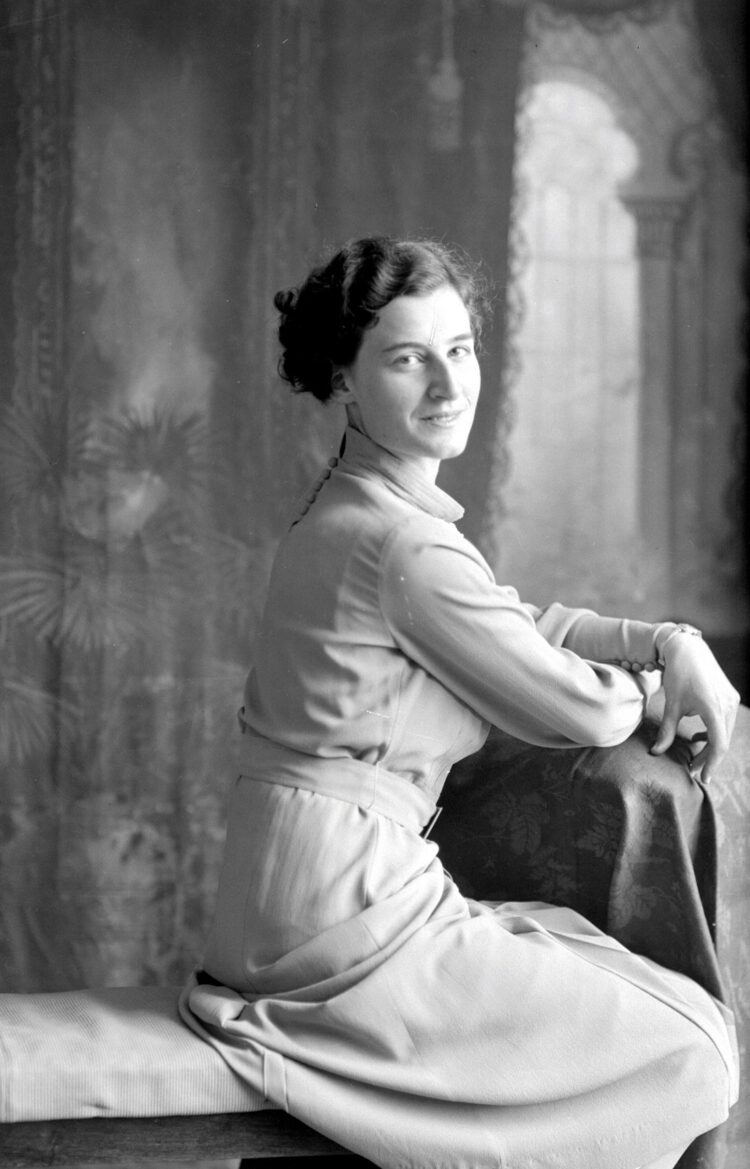 Portrait studio d'une femme assise de côté sur un banc et regardant la caméra.