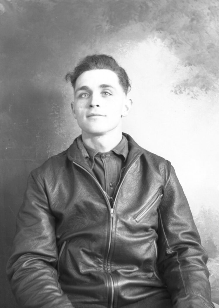 Portrait de studio, dans un décor dépouillé, d'un jeune homme portant un manteau de cuir.