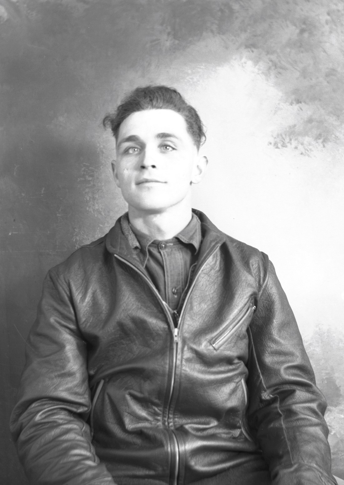 Portrait de studio, dans un décor dépouillé, d'un jeune homme portant un manteau de cuir.