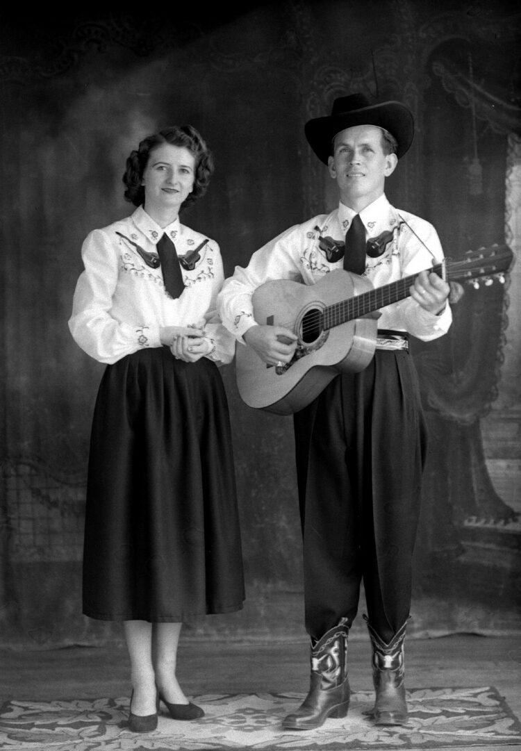 Portrait studio d'un couple en uniforme de spectacle et dont l'homme porte le chapeau de cowboy et tient une guitare dans ses mains.