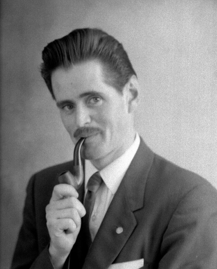 Portrait en buste en studio d'un homme élégamment vêtu et fumant la pipe.