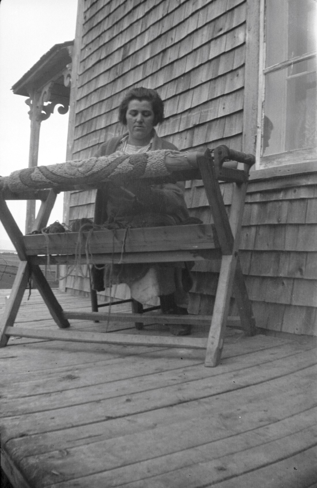 Émilia Dumont à la fabrication d'un tapis, installée sur la galerie d'une maison.