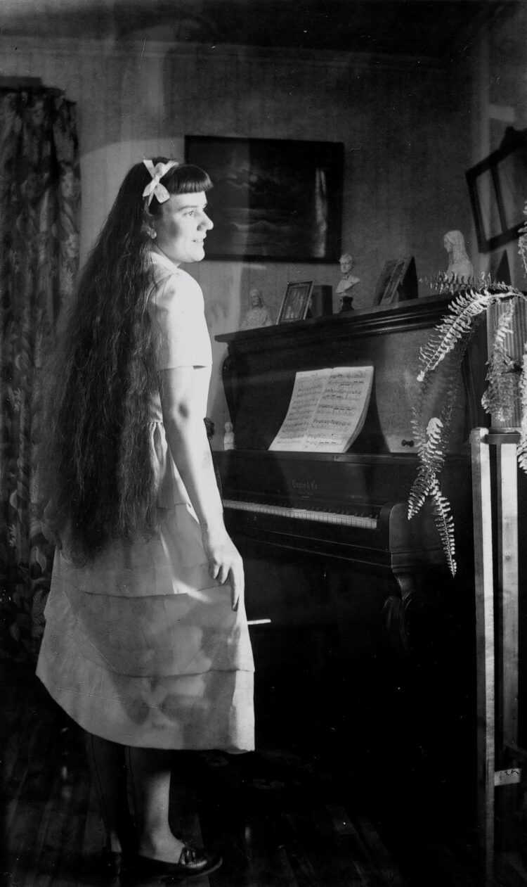 Jeune femme debout devant un piano dans un environnement domestique avec, superposée, l'image inversée sur le plan horizontal de toute la scène.