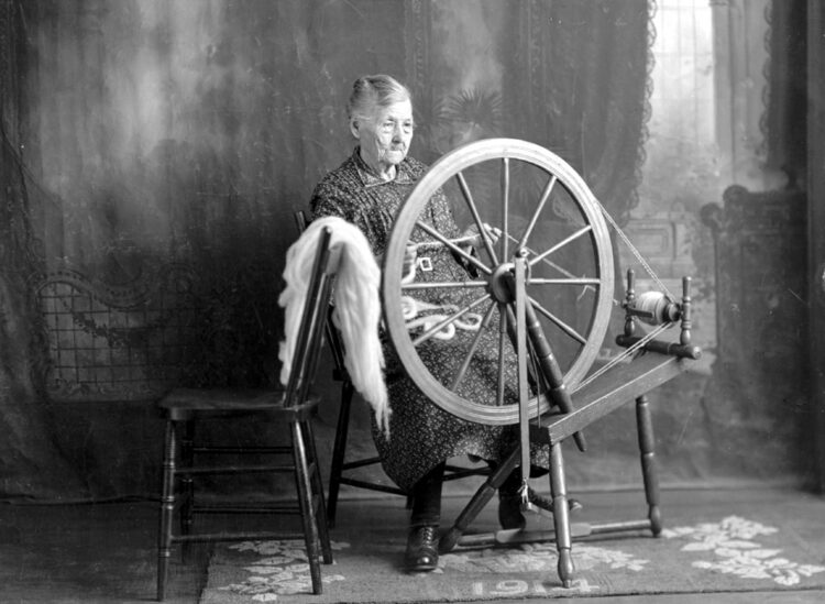 Portrait studio d'une femme âgée travaillant au rouet.