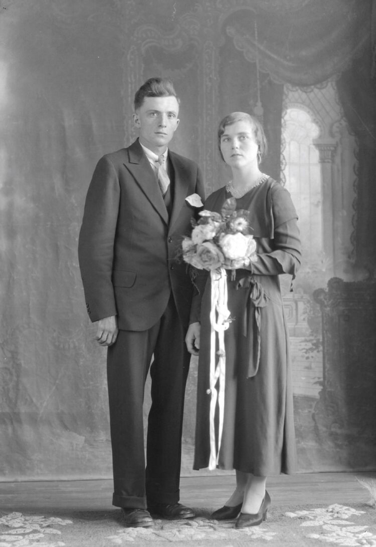 Portrait d'un couple marié en studio et dont la femme tient un bouquet de fleurs à la hauteur de sa poitrine.