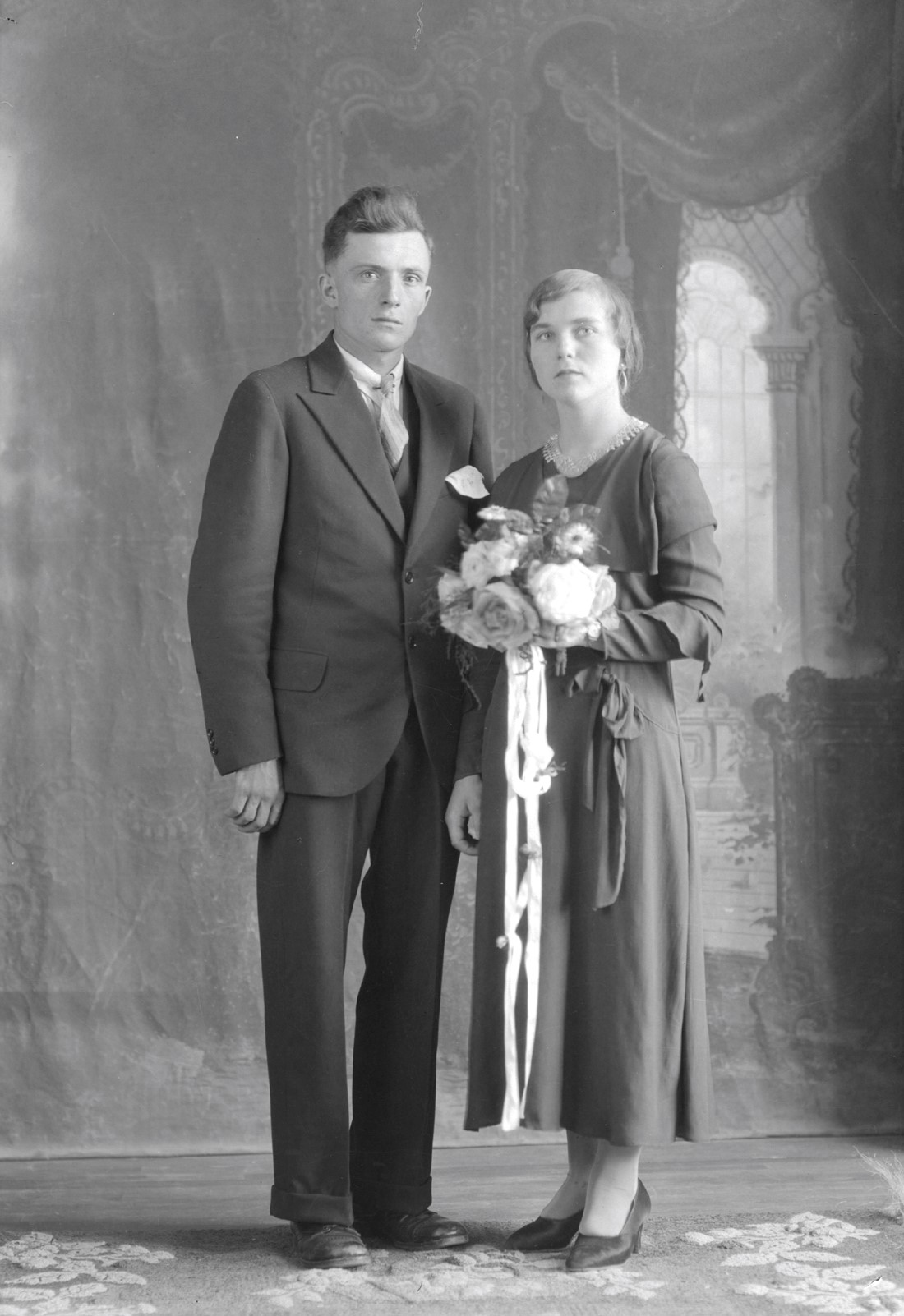 Portrait d'un couple marié en studio et dont la femme tient un bouquet de fleurs à la hauteur de sa poitrine.
