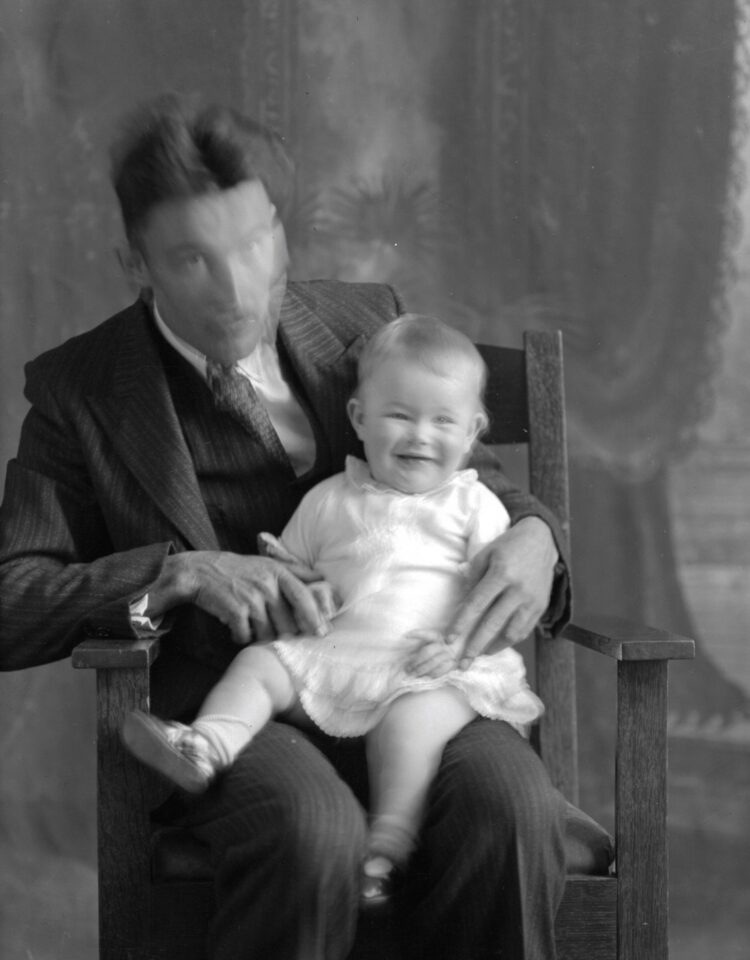 Portrait studio d'un homme avec sur ses genoux un bébé souriant dans un cliché au rendu flou.