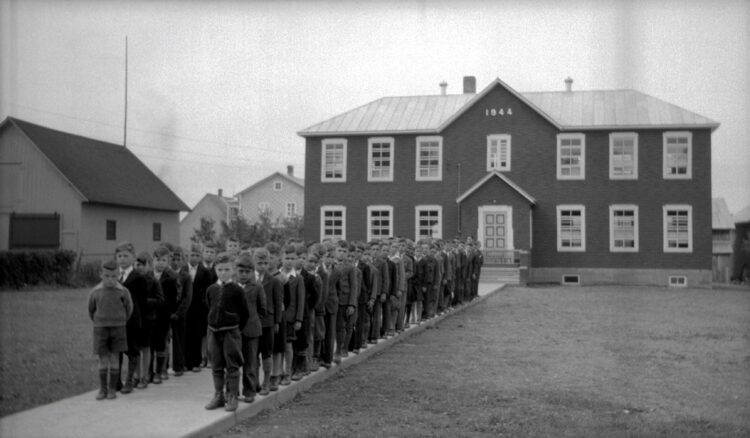 Une soixante de jeunes garçons placés en deux rangs devant une école.