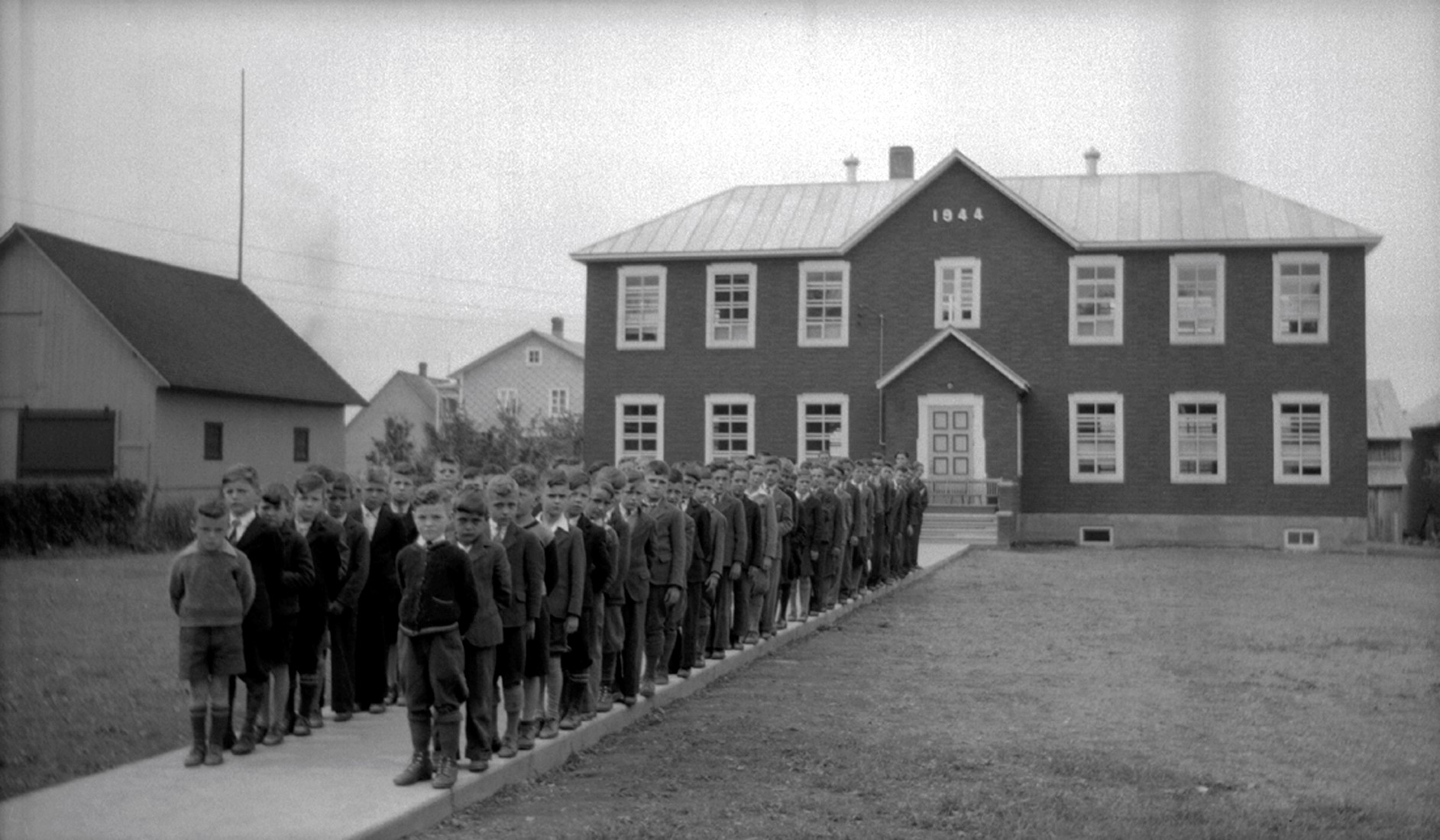 Une soixante de jeunes garçons placés en deux rangs devant une école.