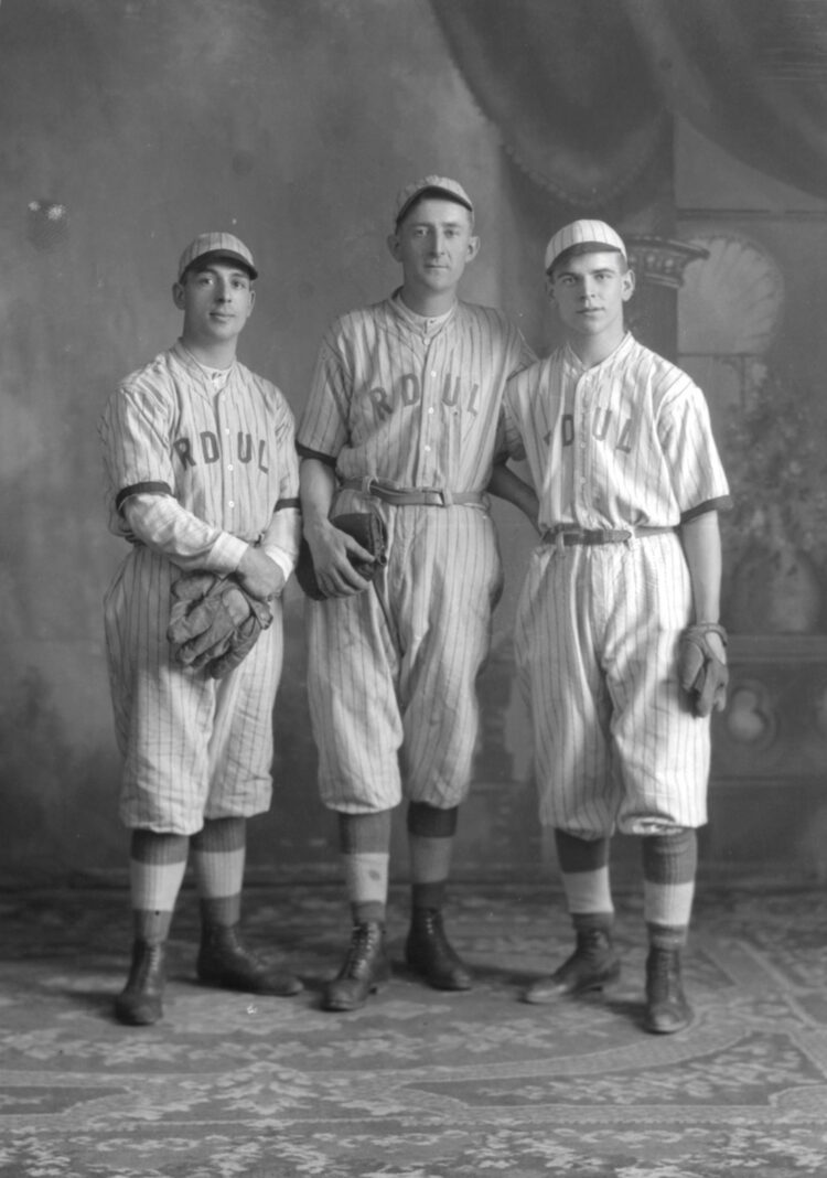 Portrait en studio de trois hommes en uniforme de baseball sur lequel est inscrit "RDUL".