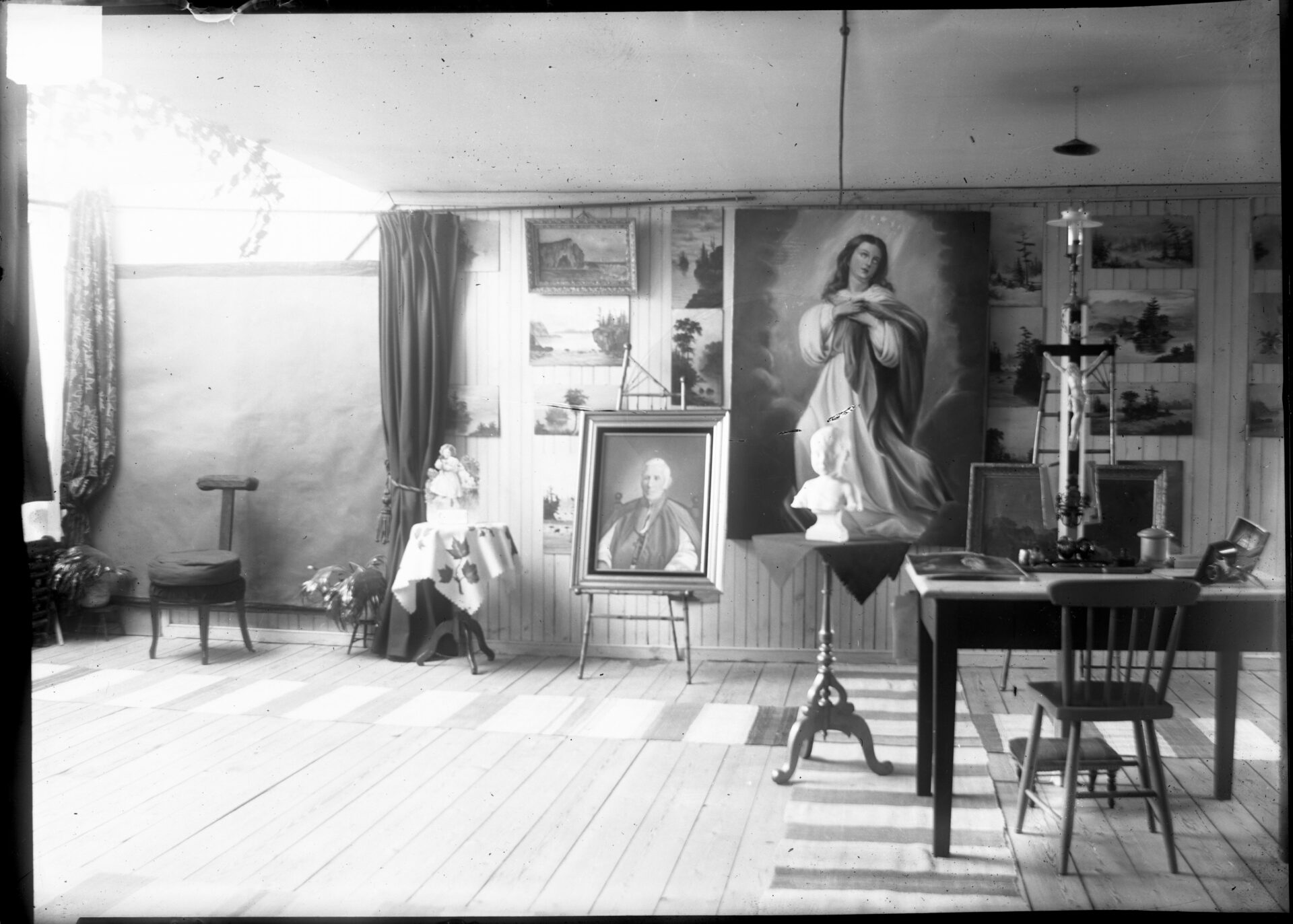 Un atelier de peinture avec plusieurs tableaux et comprenant un petit espace pour la réalisation de portraits photographiques.