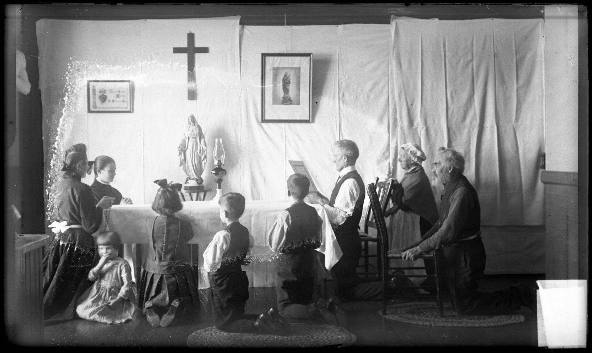 Une famille nombreuse agenouillée à la table de cuisine pour la prière du soir.