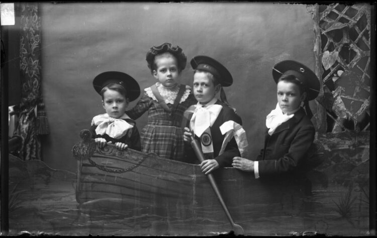 Portrait en studio d'une fillette et de trois garçons dans un canot disposé en trompe-l'œil.