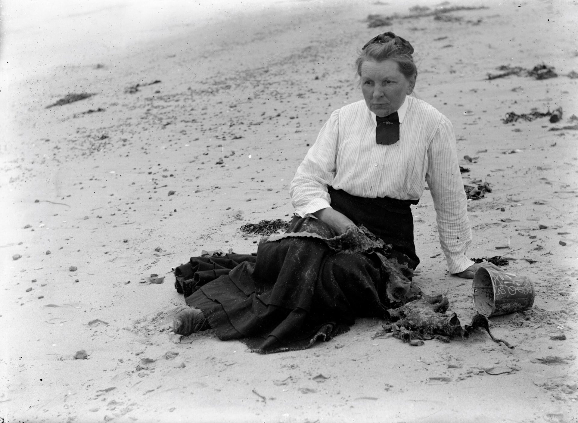 Sally Wood sur la plage vêtue d'une jupe foncée et d'une chemise blanche