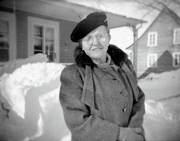 Portrait de Marie-Alice Dumont âgée d'environ 60 ans devant sa maison en hiver.