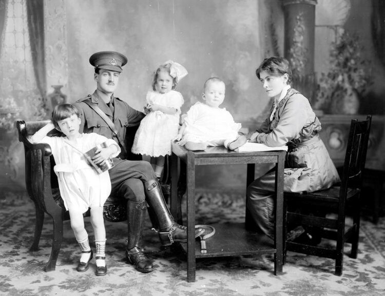 Portrait en studio d'une famille assise à table comprenant trois jeunes enfants et dont le père est en habits de militaire.
