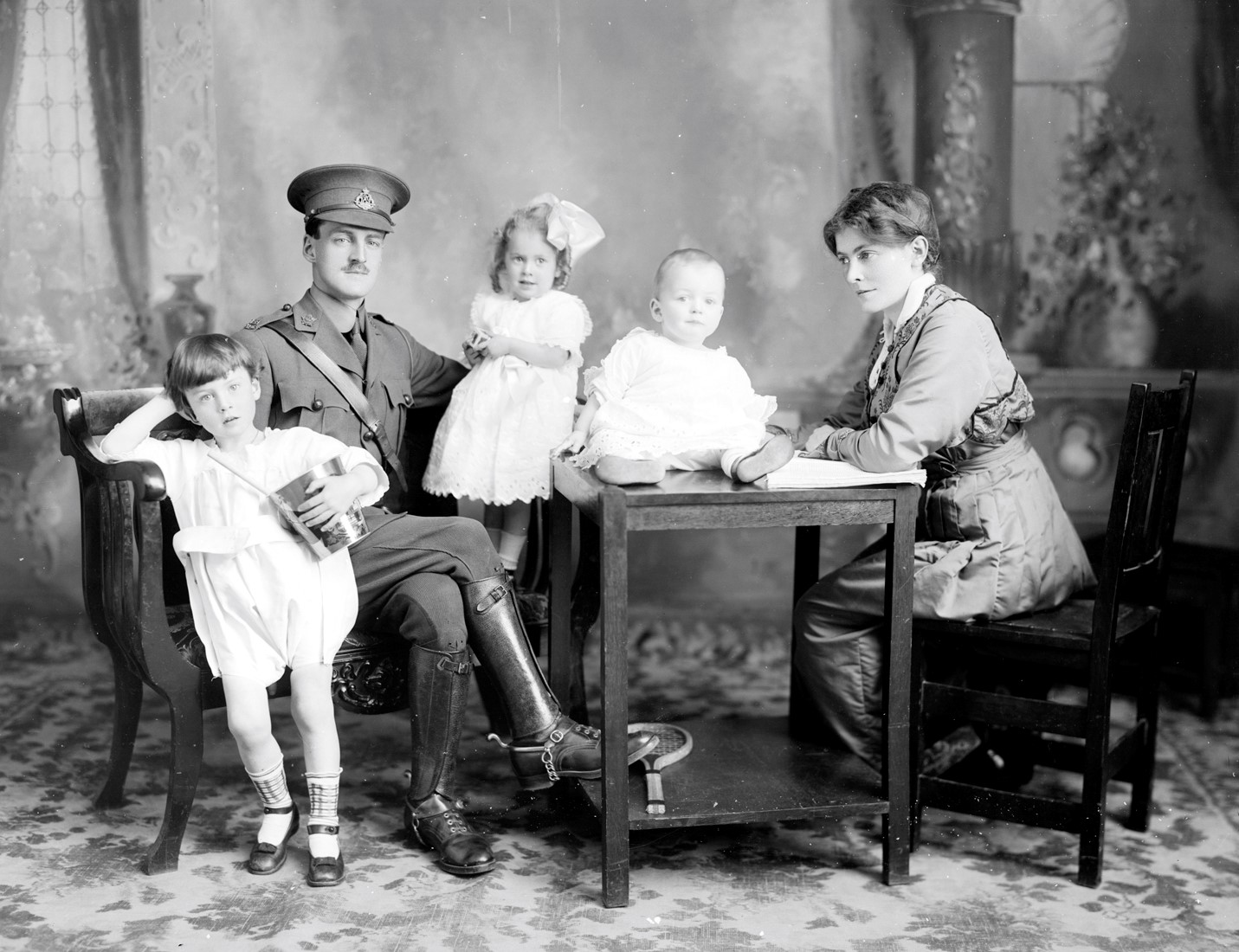Portrait en studio d'une famille assise à table comprenant trois jeunes enfants et dont le père est en habits de militaire.