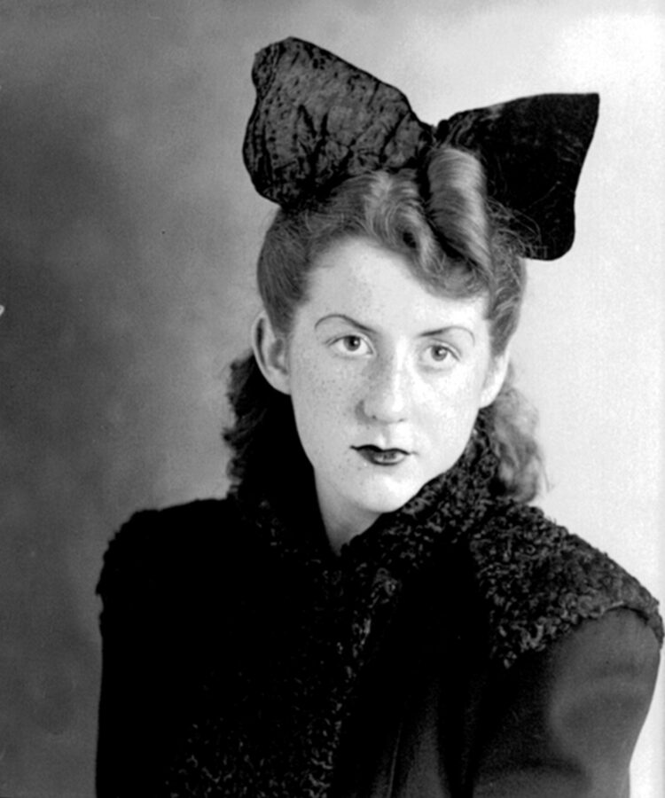 Portrait en buste, en studio, d'une jeune femme habillée d'une robe sombre et portant une grande noeud papillon en velours dans les cheveux