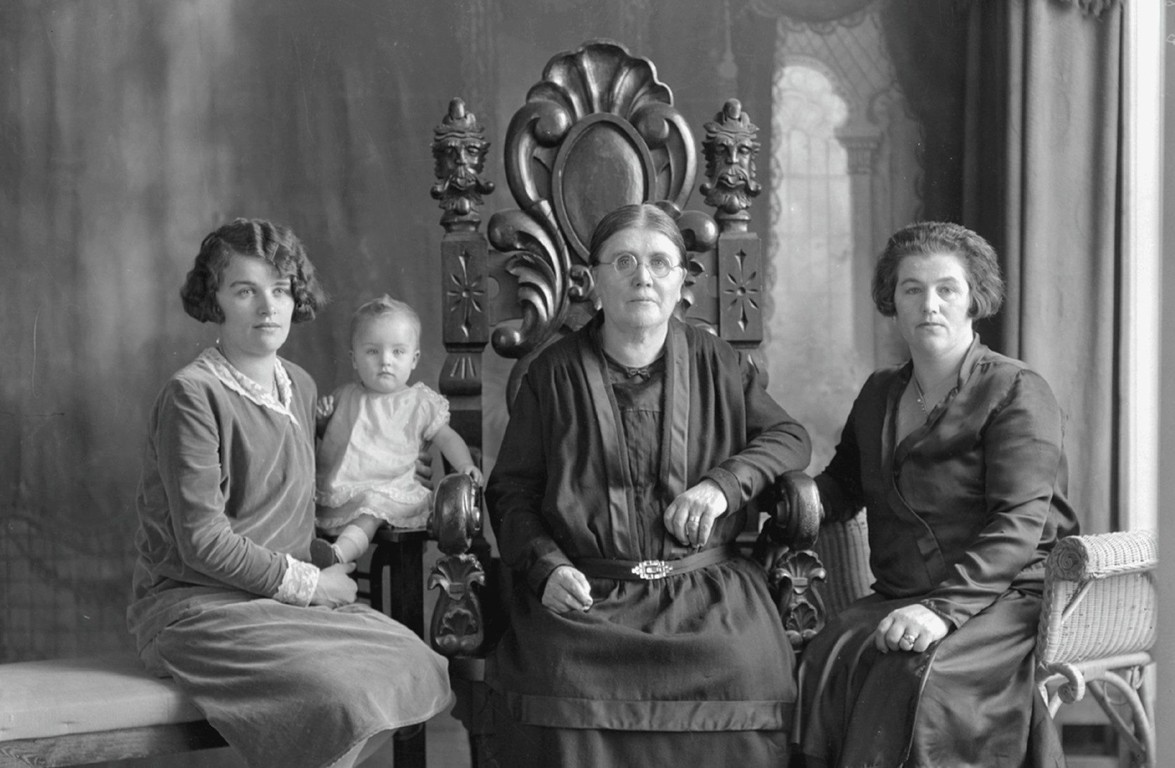 Une grand-mère, une mère, une fille et une petite-fille bébé posées en studio assises sur des chaises et un banc